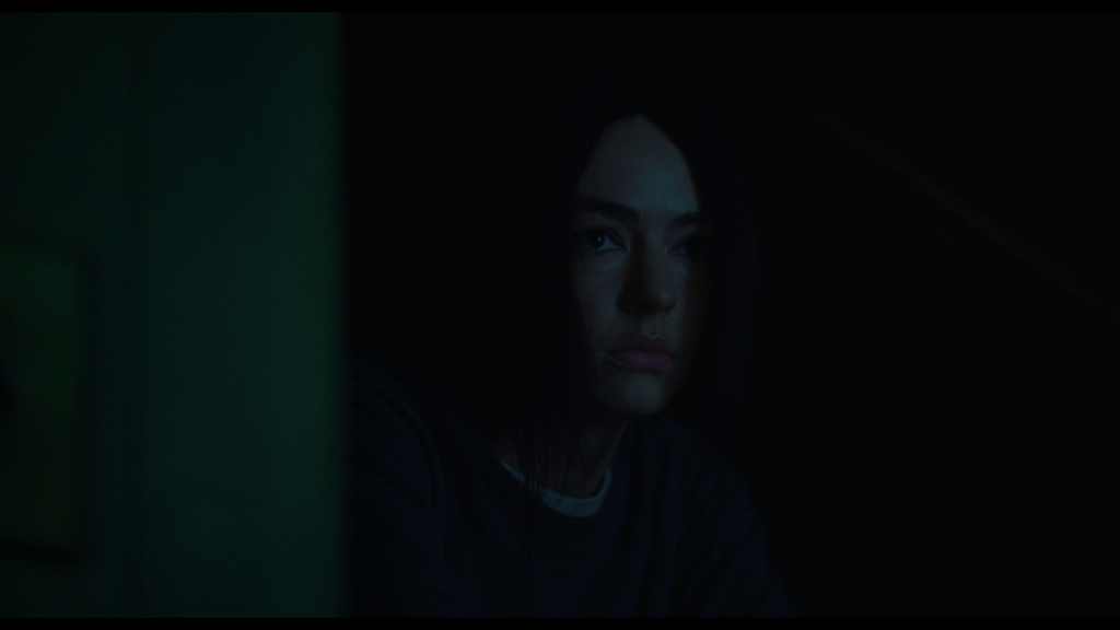 Close-up of Maddy barely visible in the darkness as she sits on her basement stairs
