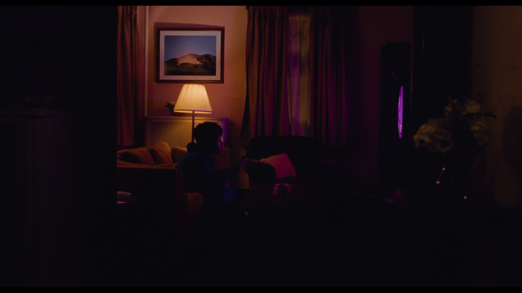 Continuation of the previous shot: the TV in the right third of the frame suddenly glows pink