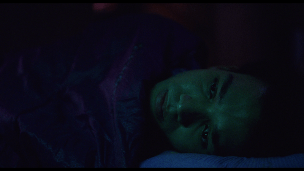 Close-up of Owen's face peaking out of a sleeping back in the lower right corner of the frame, bathed in dim green light