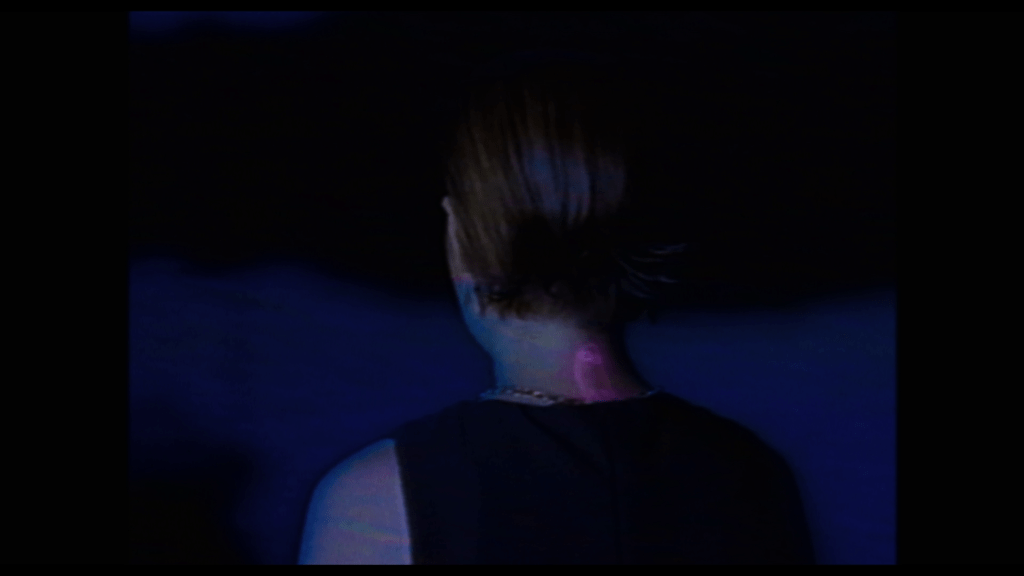 Medium close-up of the ghost birthmark on the back of Tara's neck glowing pink as she sits with her back to the camera