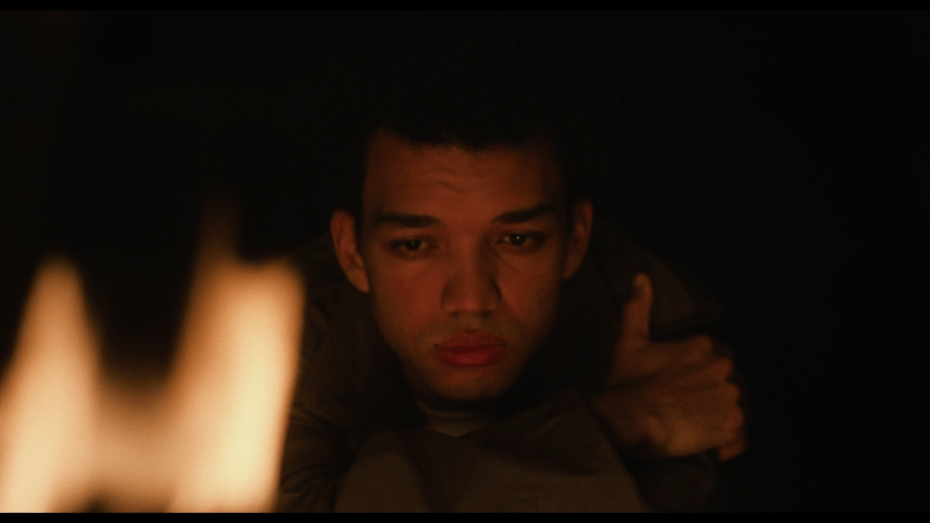 Close-up of Owen looking toward the camera through a campfire
