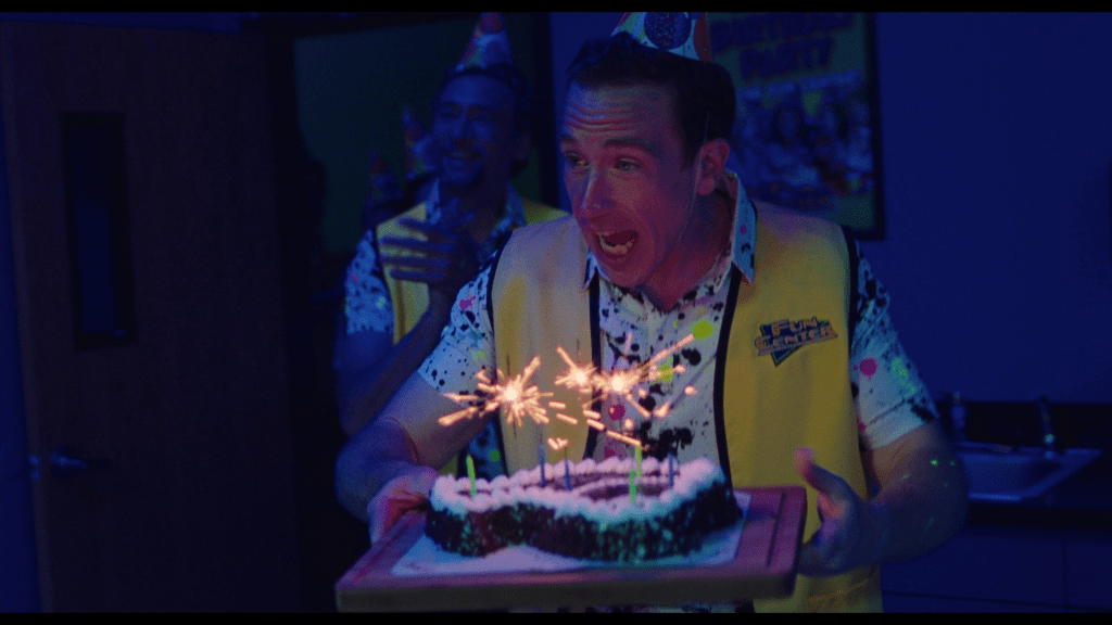 Medium shot of Dave holding a Fudgy the Whale birthday cake as Dave follows him