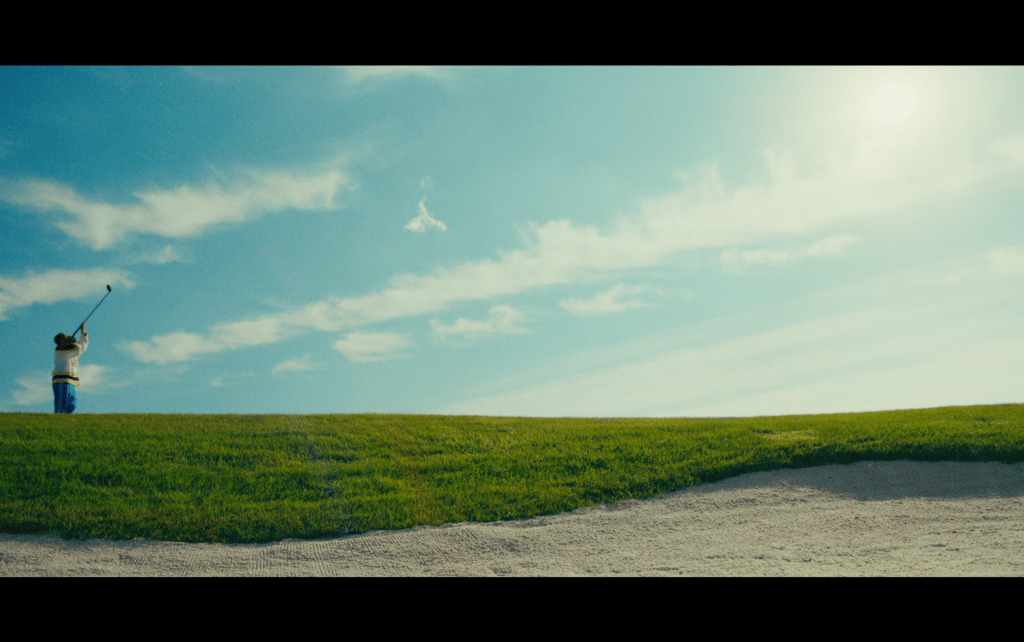 Extreme long shot of Happy Gilmore on the golf course drinking out of one of his clubs in the left of the frame as he walks past a sand trap