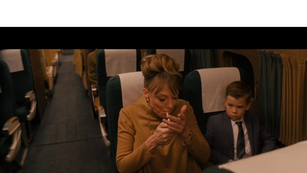 Medium shot of Clark Shotwell's Jeff looking on as his mother Helen lights a cigarette in the airplane seat next to him