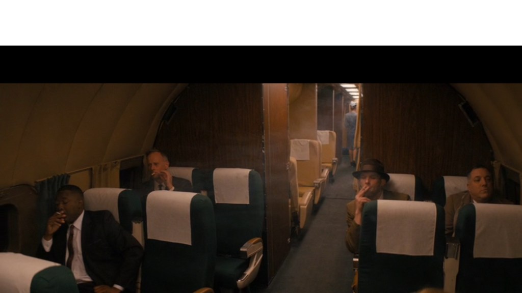 Continuation of the previous image: the camera has panned up to reveal a smoky cabin full of men also enjoying cigarettes