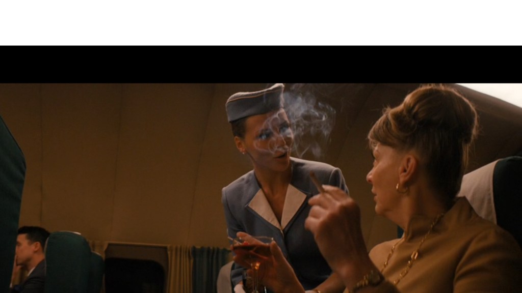 Medium shot of Olga Hoffmann's flight attendant Liz serving Helen a Manhattan in a proper coupe glass