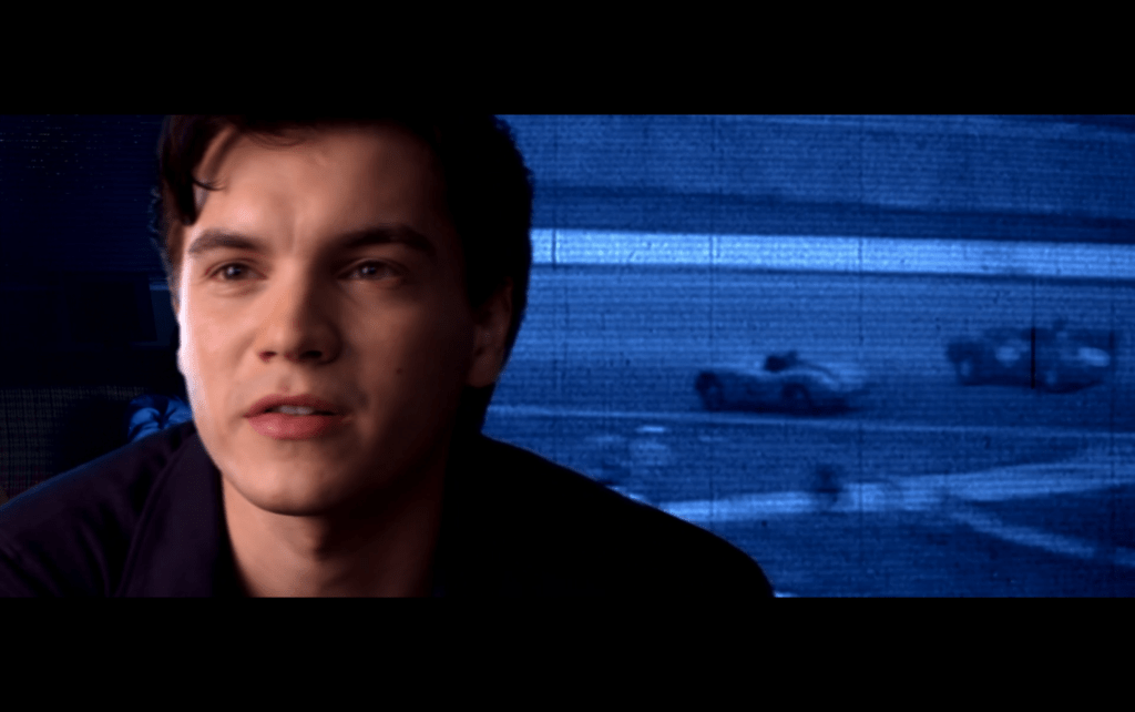 Close-up of Emile Hirsch's Speed Racer talking about the 43rd Grand Prix in front of blue-tinted black-and-white footage of the race's finish
