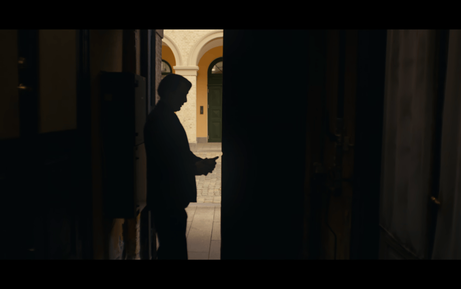 Medium long shot of Martin standing in a doorway reading a text in silhouette