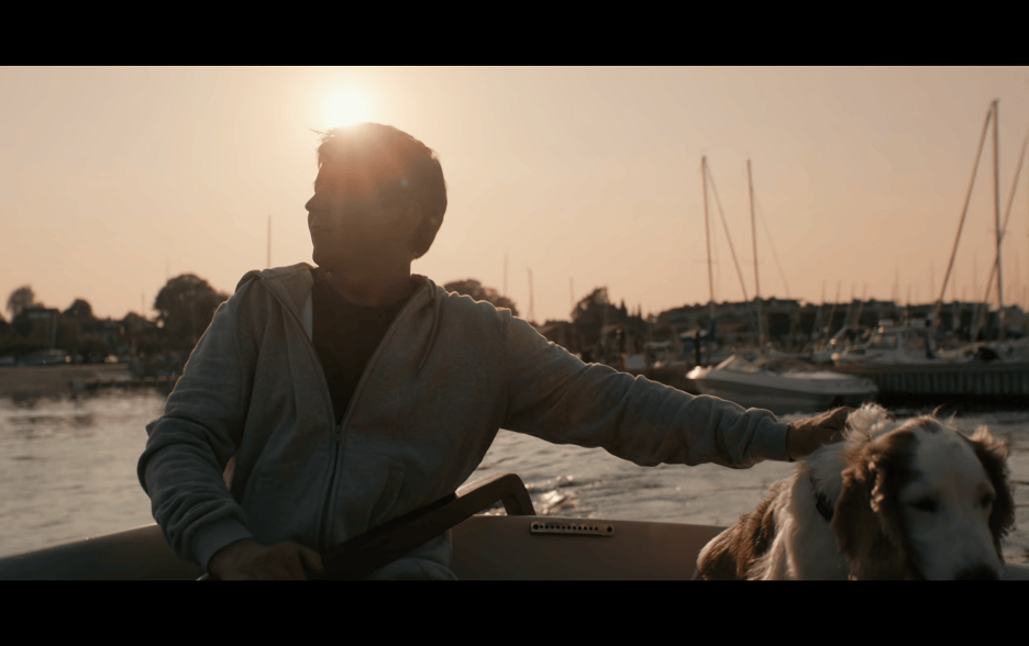 Medium close-up of Tommy on a boat with his dog positioned in front of the sun