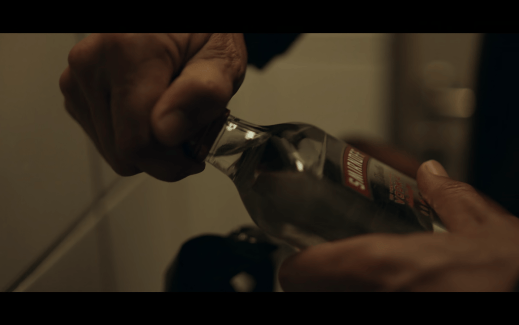 Close-up of Martin's hands unscrewing the top off a fifth of Smirnoff