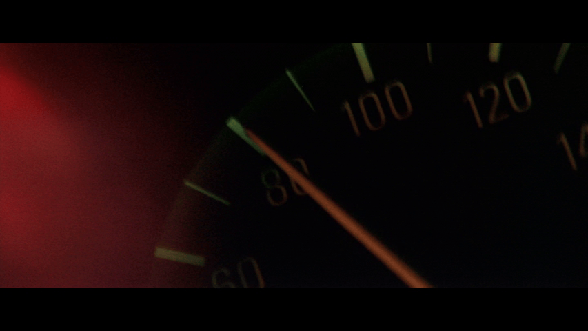 Close-up of a car's speedometer bathed in red light and reading 90 miles per hour