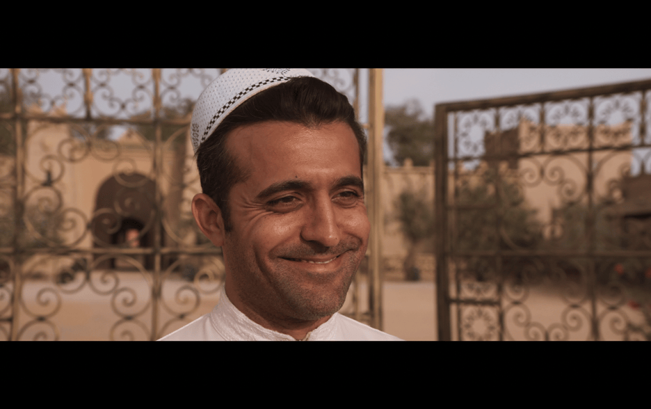 Close-up of Hamid beaming at David, who is offscreen