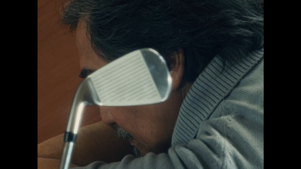 Close-up of Dr. Palanca (Teroy Guzman) asleep on his desk with the head of a golf club hovering over it
