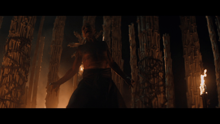 Low-angle medium close-up of Dr. Kelson disguised as Satan and dancing to the song "The Number of the Beast" by Iron Maiden in the bone temple, which is lit by torches