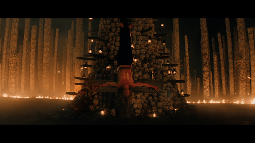 Long shot of Sir Lord Jimmy Crystal hanging upside down from a cross leaning against the tower of skulls
