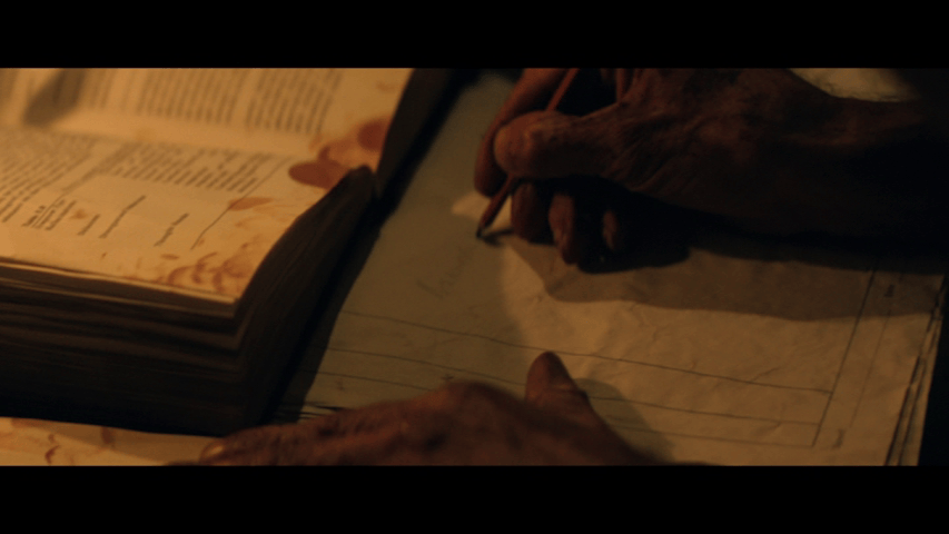Close-up of Kelson writing in one book while consulting another